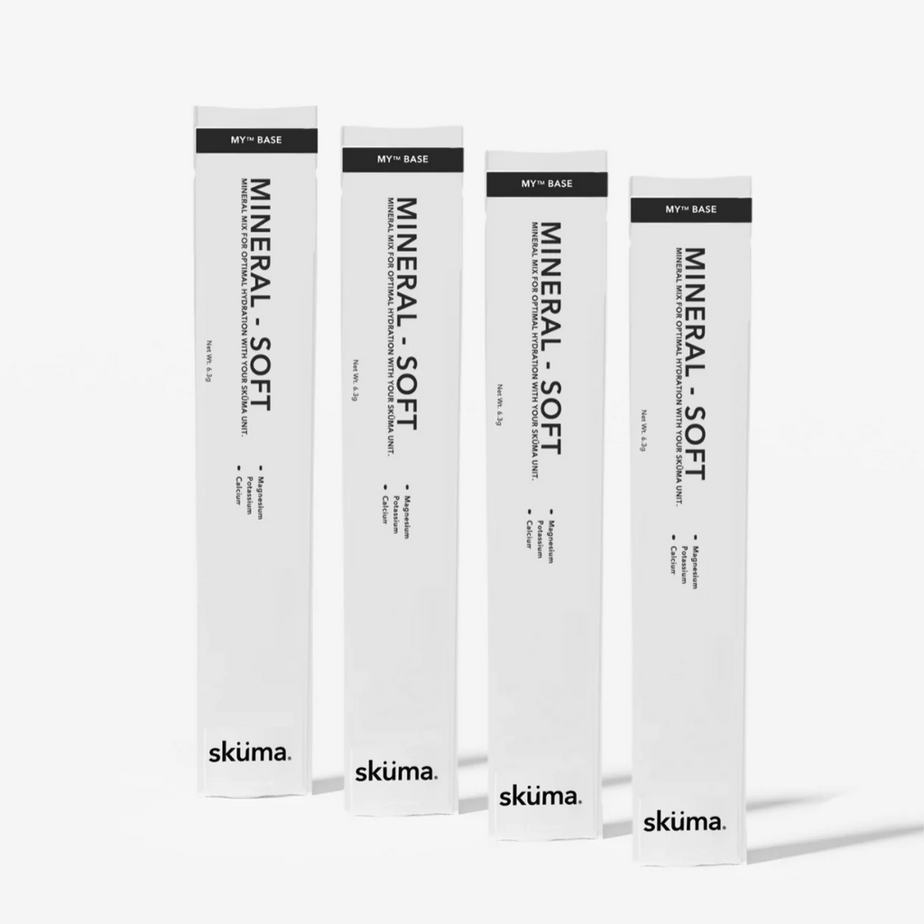 Four tall white cosmetic boxes for  Sküma. MINERAL - SOFT, arranged in a row against a light grey background.